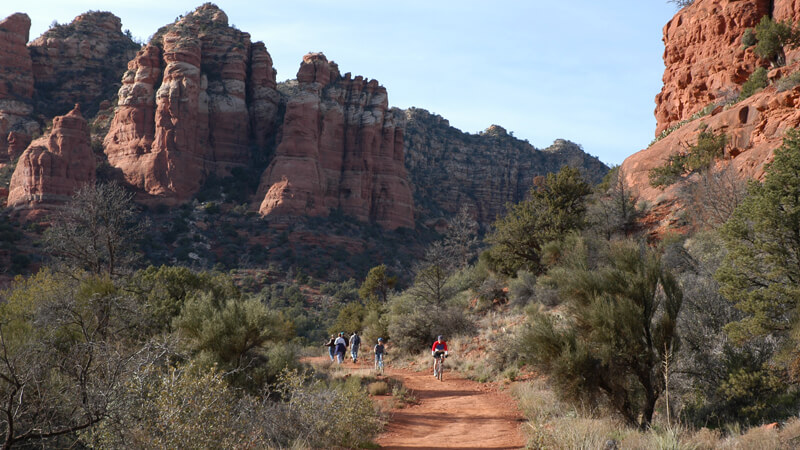 wayHiking on Bell Rock Pathway Visitors hike along the Bell Rock Pathway with the monolithic structures of red rock at their backs.